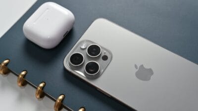 iphone 15 pro max. se ve el telefono junto a un cuaderno y unos auriculares